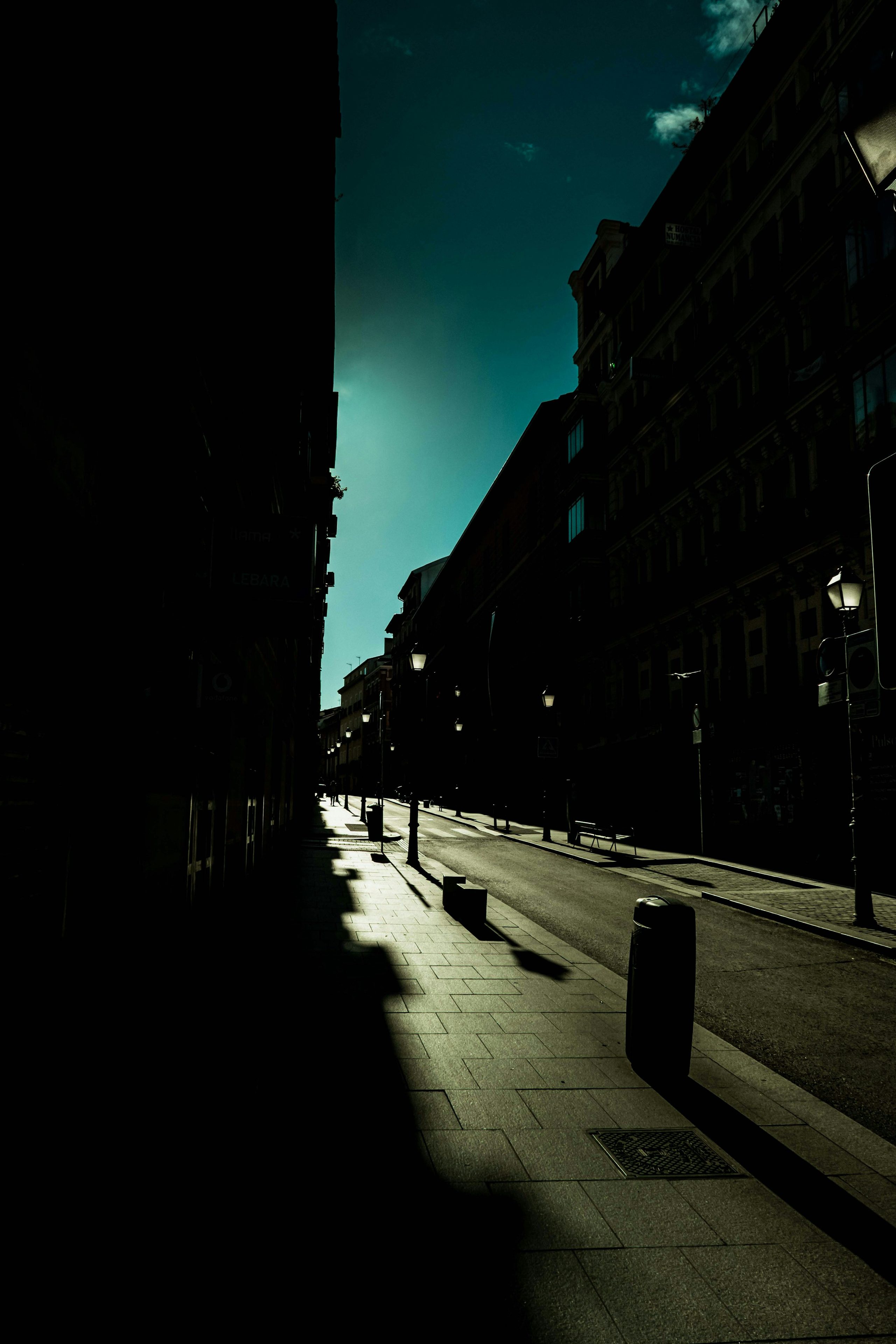 A narrow city street held in deep shade beneath a bright sky.