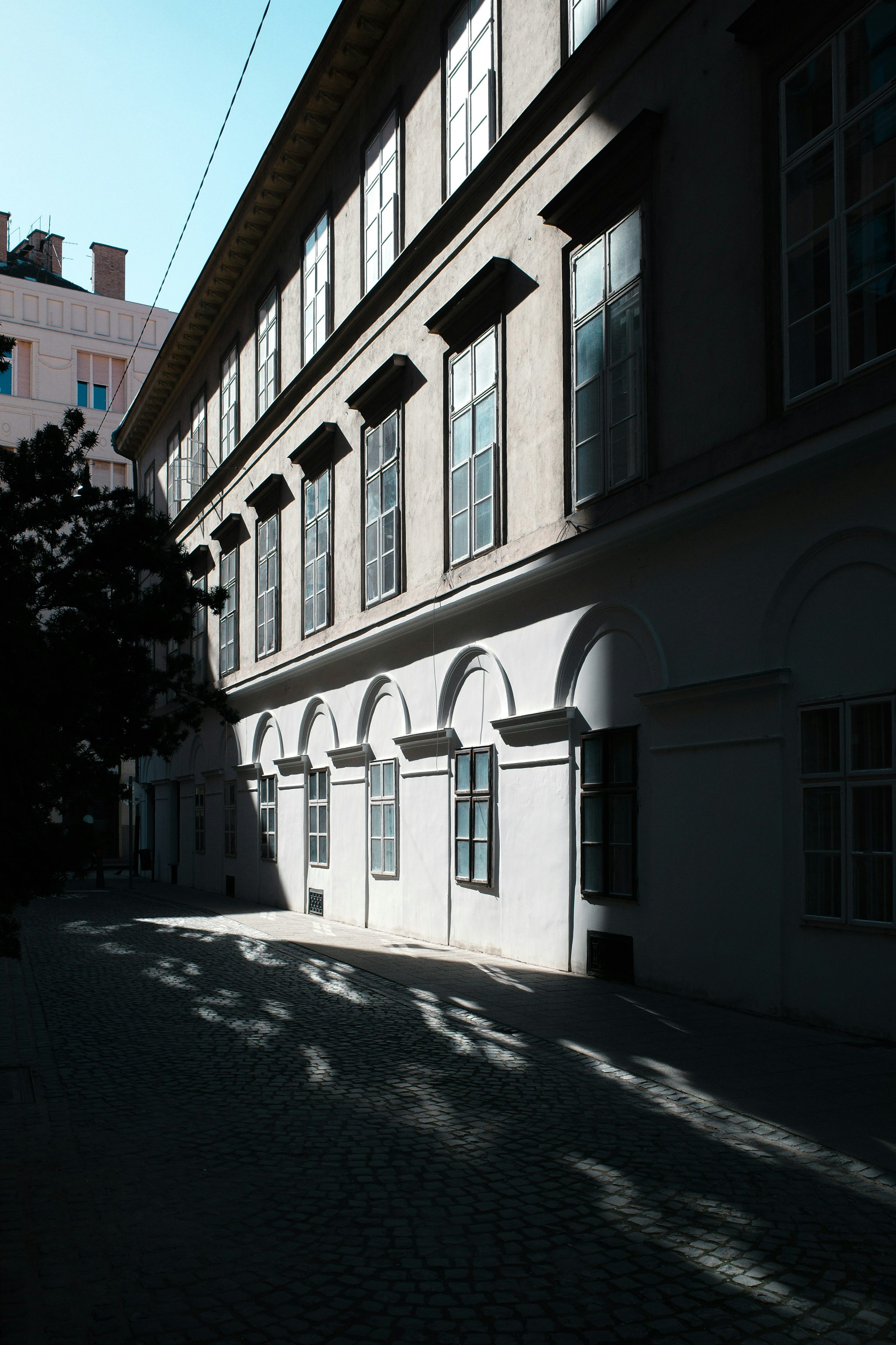Sunlight cuts diagonally across a white building and cobblestone street.