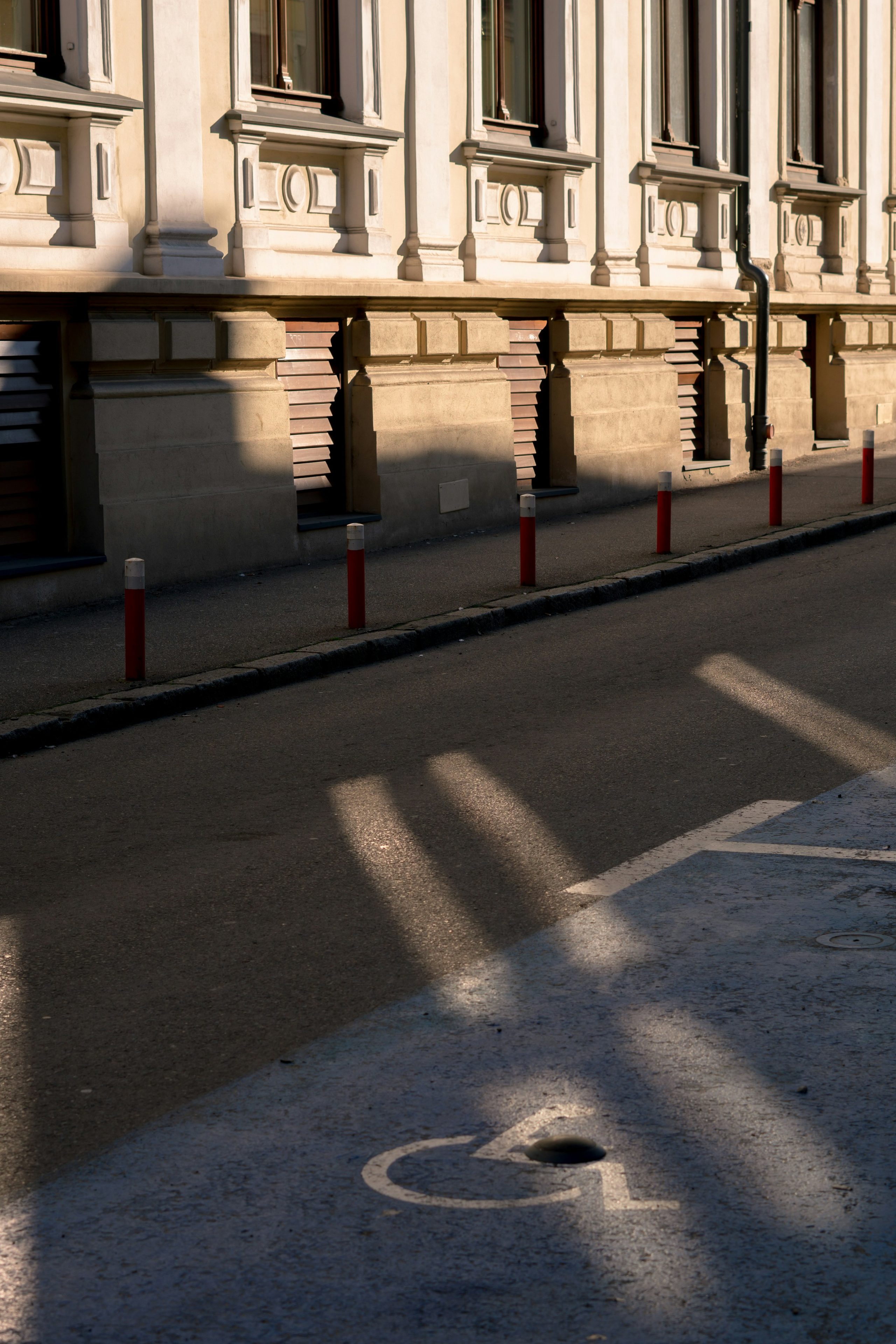 A long concrete facade and roadside bollards in warm afternoon light.