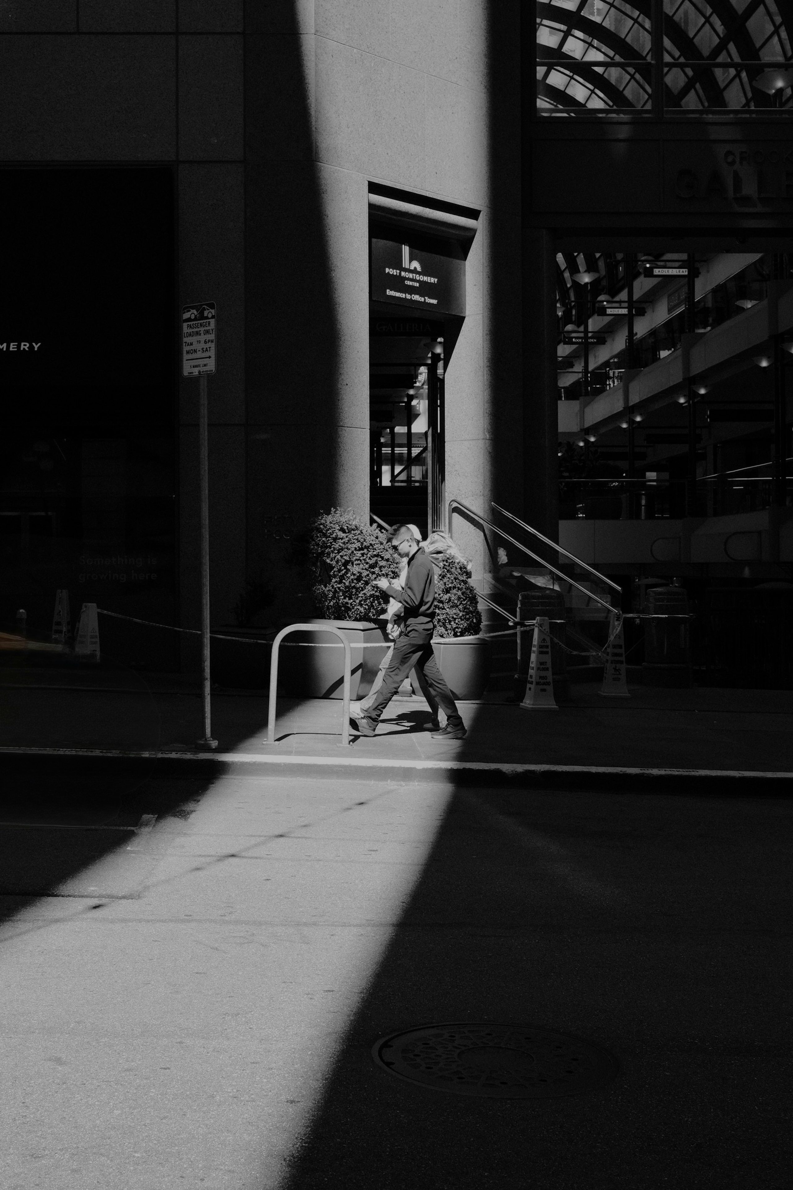 A pedestrian crosses a building entrance divided by dramatic shadows.