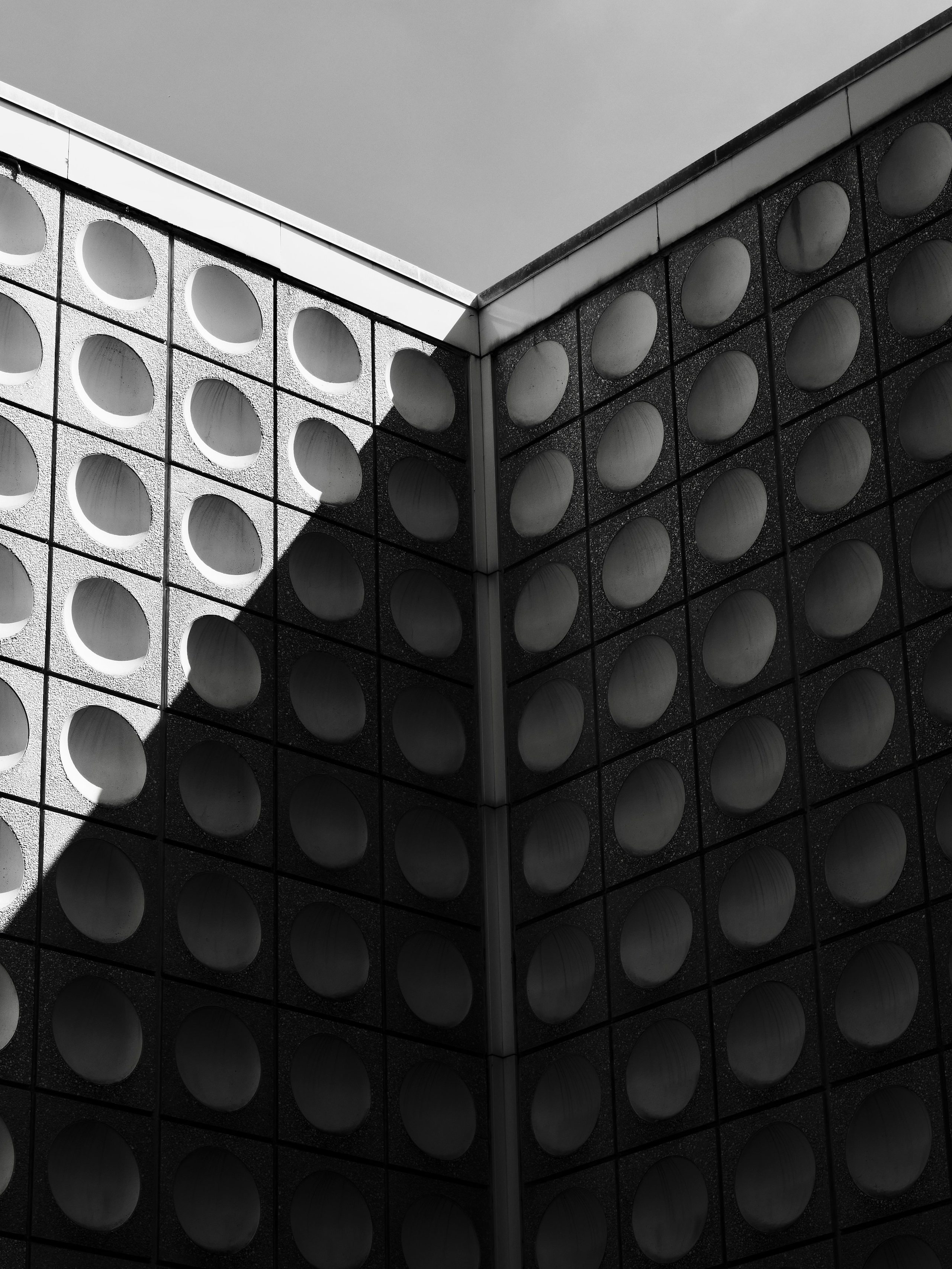 Circular patterns and sharp shadow animate a monochrome building facade.